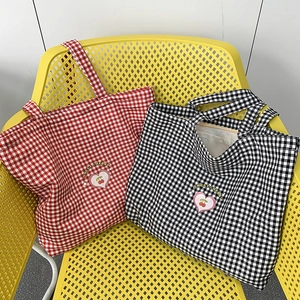 Détail de sacs cabas en toile à carreaux rouges et noirs avec broderie cerise douce