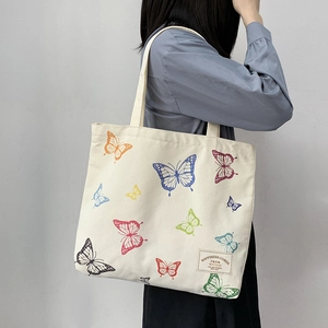 Off-white canvas tote bag featuring colorful butterfly prints and artistic textile label