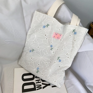 Detail of white canvas tote bag featuring floral embroidery and pink handmade label