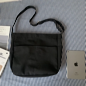 Detail of black canvas crossbody bag with dual front pockets and adjustable metal buckle strap