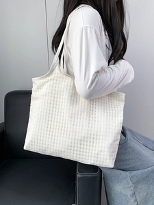 Close-up of lightweight beige gingham canvas tote bag held by a model on a leather chair