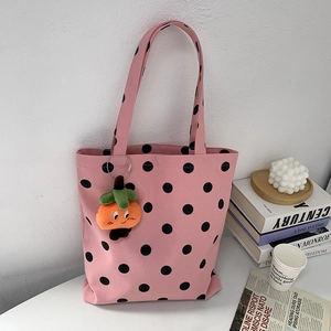 Pink canvas tote bag with white polka dots featuring an orange pumpkin plush charm detail