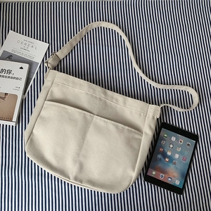 Detail view of large cream canvas crossbody bag with dual front pockets and adjustable strap