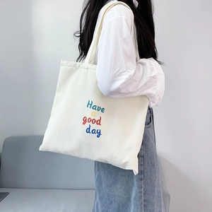 Detail of white canvas tote bag with 'Have a good day' text on model's shoulder