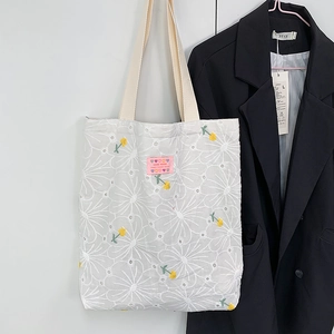 Detail of white canvas tote bag with daisy floral embroidery and pink handmade label