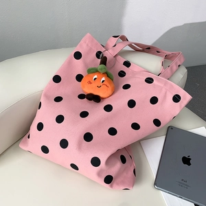 Pink canvas tote bag detail with large black polka dots and orange plush persimmon charm