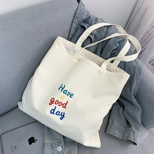Close-up of a white canvas tote bag with 'Have a good day' text and a top zipper closure