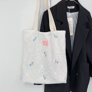 Detail of white lace embroidery tote bag featuring blue-green floral patterns and handmade label