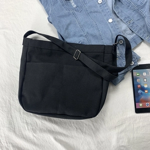 Detail of black canvas crossbody bag featuring front double pockets and adjustable strap