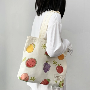 Detail of canvas tote bag showing colorful fruit prints and artistic label on a white strap