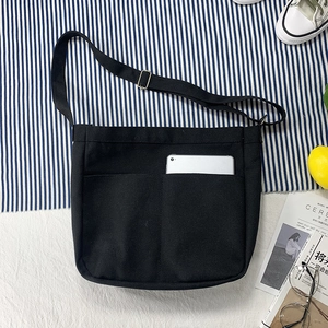 Detail of black canvas crossbody bag featuring dual large front pockets and adjustable strap