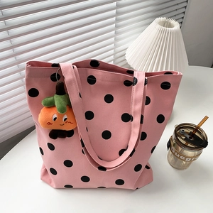 Pink polka dot canvas tote bag detail with cute orange plush charm on white table
