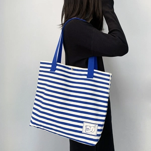 Close-up of blue striped canvas tote bag showing metal snap button and cute bear patch