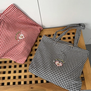 Détail de sacs en toile à carreaux rouges et noirs avec broderie cerise et poignées