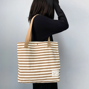 Detail of striped canvas tote bag with brown straps and cute bear embroidery patch