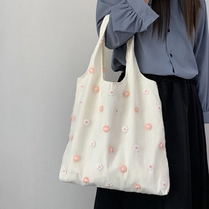 Détail d'un sac cabas en toile avec appliques de marguerites 3D porté par un mannequin