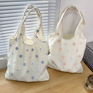 Détail de sacs cabas en toile avec broderie florale 3D sur une surface en bois clair