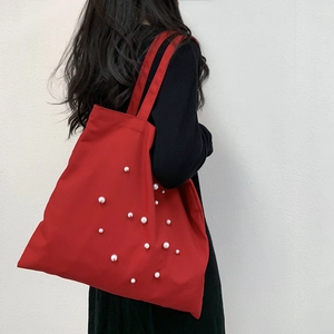Detail of red canvas tote bag featuring elegant white pearl embellishments and large capacity