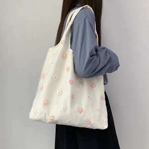 Gros plan du sac fourre-tout en toile crème avec broderies florales 3D et bandoulières