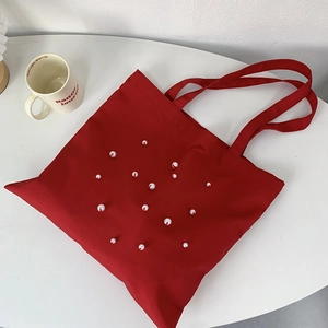Detail of red canvas tote bag with white pearl heart pattern on a white tabletop