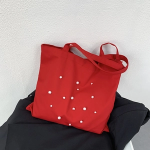Detail of red canvas tote bag with elegant white pearl embellishments and sturdy handles