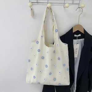 Détail de broderies florales bleues et blanches sur un sac à main en toile blanc cassé