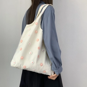 Détail de la broderie florale sur un sac cabas en toile blanche porté par un mannequin