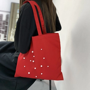 Detail showing red canvas tote bag with pearl accents worn by model on shoulder