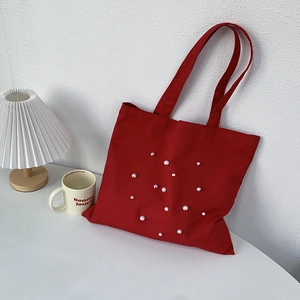 Detail of red canvas tote bag with pearl accents on a minimalist white desk setup