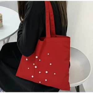 Detail of red canvas tote bag with white pearl accents shown on model's shoulder