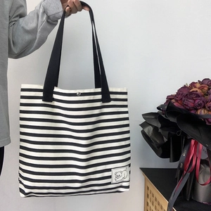 Detail of striped canvas tote bag featuring silver snap button and cartoon cat patch label
