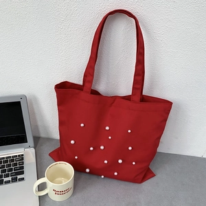 Close-up of red canvas tote bag featuring decorative white faux pearl rivet details