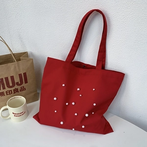 Close-up of red canvas tote bag with pearl accents and a snap button closure