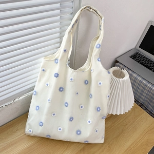 Détail du sac cabas en mesh blanc avec broderie florale bleue sur fond en bois