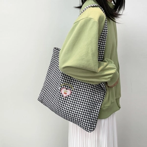 Détail du sac cabas en toile à carreaux avec broderie cerise sur l'épaule du mannequin