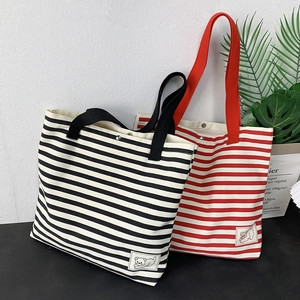 Detail of striped canvas tote bag featuring secure metal snap button and bear patch decoration