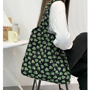 Detail of large black corduroy tote bag with green heart patterns worn by a model