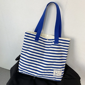 Detailed close-up of striped canvas tote bag with polar bear patch and blue handles