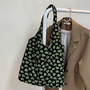 Detail of black tote bag with green heart patterns hanging on a rack with a blazer