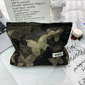 Detail of a large makeup bag with gold butterfly embroidery and logo set on a desk