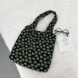 Detail of green heart patterns on black canvas tote bag with glasses on white background