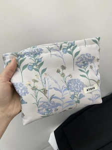 Detailed close-up of the elegant purple hydrangea floral embroidery on the beige makeup bag