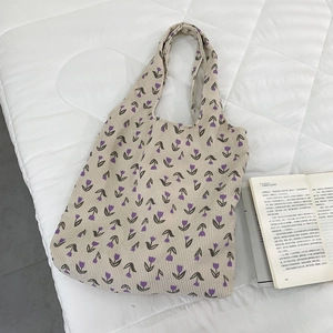 Close-up of beige corduroy tote bag featuring purple tulip floral patterns on soft bedding