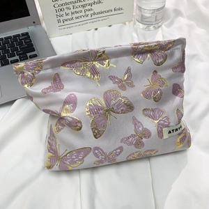 Close-up of golden butterfly embroidery on light purple fabric cosmetic bag with brand tag