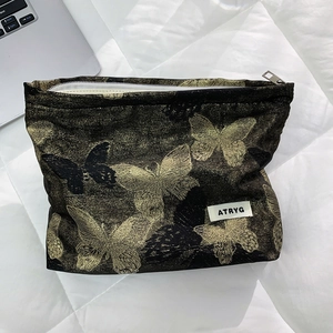 Macro shot of gold butterfly brocade makeup bag with ATRYG label on white surface