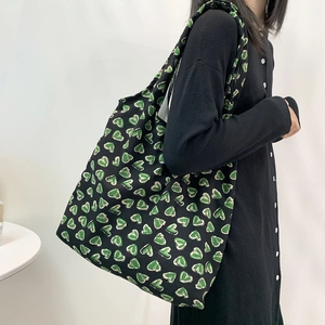 Detail of a large capacity canvas shoulder bag featuring green hand-drawn heart prints