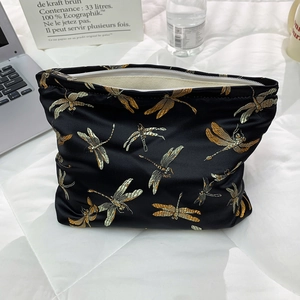 Detailed close-up of a large black makeup bag featuring delicate dragonfly embroidery