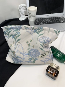 Detail of jacquard makeup bag with blue floral patterns and brand logo in lifestyle setting