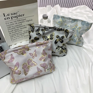 Detailed close-up of three butterfly toiletry bags in pink, grey, and blue with gold accents
