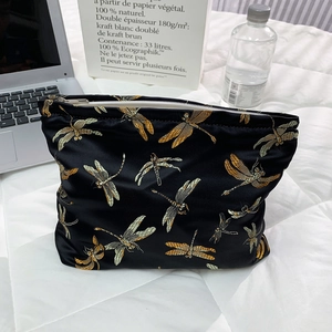 Detailed close-up of golden dragonfly embroidery on a black satin cosmetic bag texture